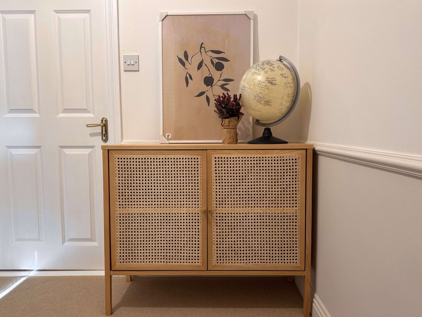 A light coloured wooden cabinet with rattan doors. A white and grey globe sits on top. 