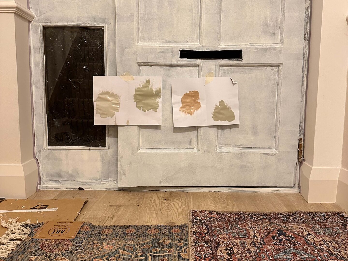 A front door with paint samples and two floral rugs on the ground.